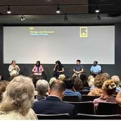 Audience looking at 5 people sitting on stage.