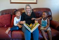 IRC volunteer reads to two children on the couch