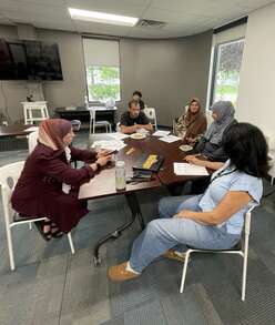 A group of five adults--four women and a man--sit at a table participating in a parenting workshop.
