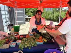 A young woman wearing glasses sells fresh vegetables at a farm stand.