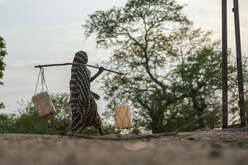 En flicka går med hinkar för att hämta vatten. 