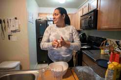 A women stands at the kitchen counter rolling dough in her hands. 