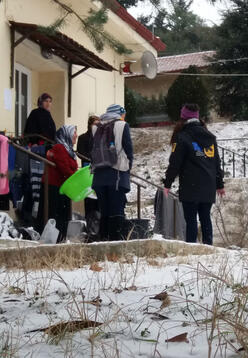 IRC aid workers speak with refugees outside a building in the Veria refugee site in northern Greece after a snowfall.