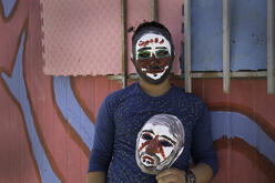 A young Syrian refugee wears and carries masks he painted at an IRC workshop