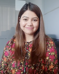 Huzan is wearing a red flowery blouse and is smiling at the camera