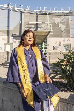DACA recipient Lupe wearing her UC, Merced college graduation robes outside a building in her San Diego neighborhood