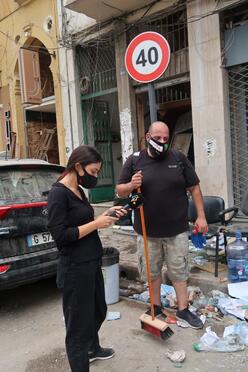 Elias El Beam holds a broom while another volunteer checks her phone as they help clear debris after the Beirut explosion