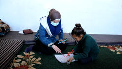 IRC counselor Fadia and 8-year-old Reem sit on a carpet looking at Reem's drawing pad.