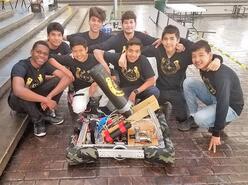 The robotics team sitting and posing around their creation.