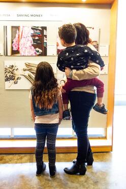 Women holds young child and stands with other child, all looking at photos