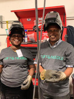 Two people inside a factory smile for a photo with their protective gear.