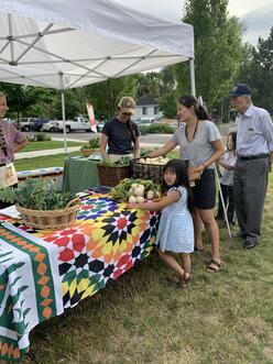 Customers viewing farmers market produce with staff volunteers in the background.