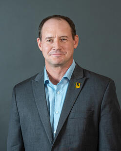 A man in a suit with an IRC pin smiles for a photo after being named the new Executive Director for IRC