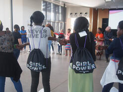 Girls with "girl power" bags stand in a circle holding hands as part of an activity