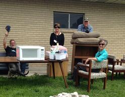 Members of the refugee resettlement committee sitting outside a home on donated chairs and cushions.