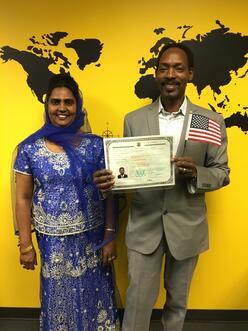 Two individuals standing while the man holds his United States citizenship paper and U.S. flag.