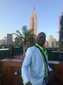 Man in white suit posing at a rooftop restaurant in front of the Empire State Building in New York.
