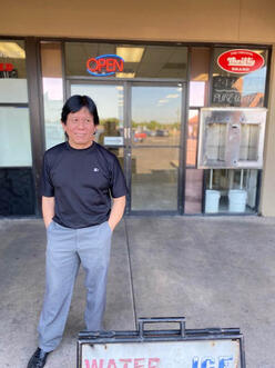 A man standing in front of a storefront with an open sign