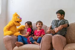 Jad, a furry Muppet character from the new Sesame Street show for refugees, Ahlan Simsim, with three laughing Syrian children