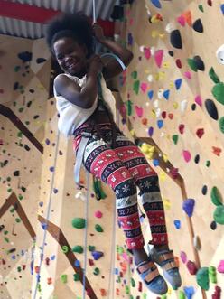 Girl descending from a rock climbing wall on a rope, smiling.
