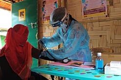 Wearing full PPE, including a face shield, a midwife takes the blood pressure of a patient. 