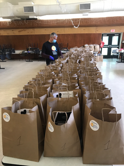 Jas preparing for distribution next to 2 large rows of food in bags on a table