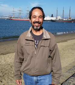 Online youth tutor, Dave, standing for a photo with a beach and boats in the background.