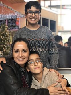Meheria Habibi has her arm around one of her sons while another one of her sons stands behind her. All three are smiling and looking at the camera. 