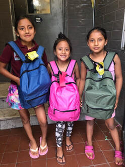 3 students carrying their new backpack with learning supplies. 