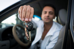 A man sitting in the drivers seat of a car holds up car keys.