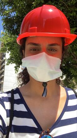 A selfie photo taken by Rebecca Mouawad. She is wearing a red hard hat and a white surgical mask. 