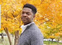 Artist looking into the camera with fall trees in the background in a park.