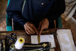 Closeup of Wa'ad's hands as she measures fabric for COVID-19 face masks in Syria.