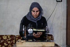 Um Abdo sits at a sewing machine to make COVID-19 masks in Syria