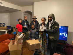 A family of six stands in their living room with the light one candle items they received, 