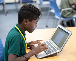 A young boy works on a laptop computer in a classroom.