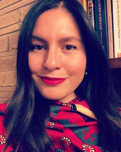 A woman wearing red lipstick smiles, with a bookcase in the background.