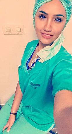 Dr. Rose M. Al-Nsour, wearing blue scrubs, smiles and takes a selfie photo