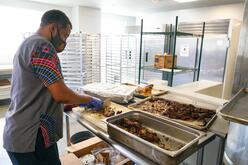 Chef Abudu cuts meat in his kitchen, looking down at the cuttingboard.