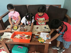 Children sit on a couch drawing pictures and playing games at a coffee table