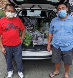 Two men stand in front of a vehicle packed with fresh produce