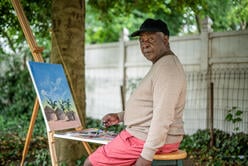 Artist Muyambo Marcel Chishimba paints a landscape at his easel in his New Jersey backyard. 