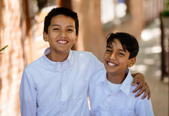 Leander and Jesus, both wearing white button-up shirts, smile widely to the camera with their arms around each other.