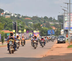 Boda Bodas—motorbike taxis—ride on a wide Kampala street, some carrying passengers.