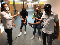 Three IRC staff members and Milad stand in the hallway of a school, testing the microphone and video equpment