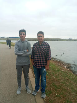 Ehsanullah and his son stand in front of a body of water 