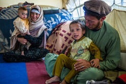 A father and mother from a farming family who were displaced by drought hold their small childen in their laps as they sit on the floor of their tent in Badghis, Afghanistan..