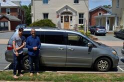 Two men stand in front of a silver minivan they have just received
