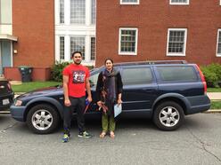 A man and woman stand in front of a black station wagon