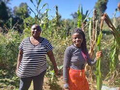 Two women stand in front of corn stalks at a New Roots garden in Charlottesville